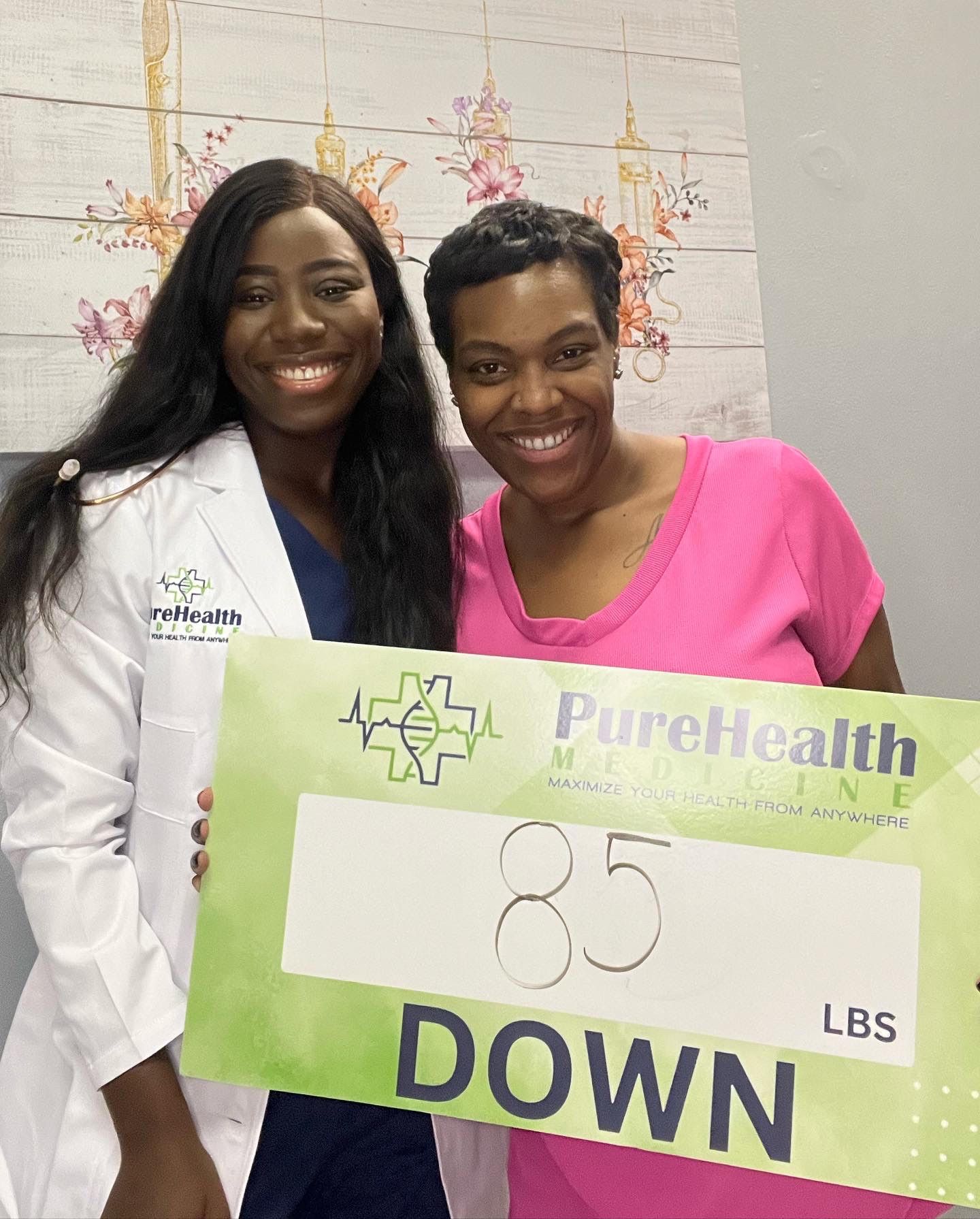 Two smiling women hold a green PureHealth sign reading “85 LBS DOWN.”