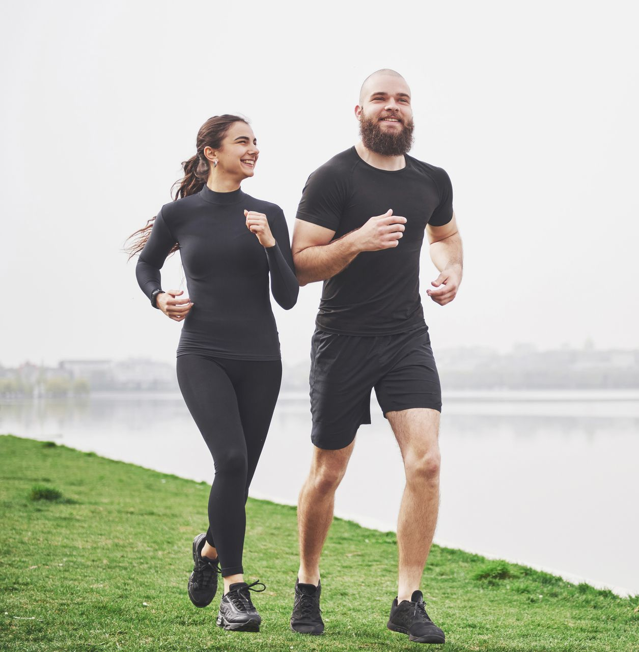 a man and a woman in black clothes are jogging by the lake