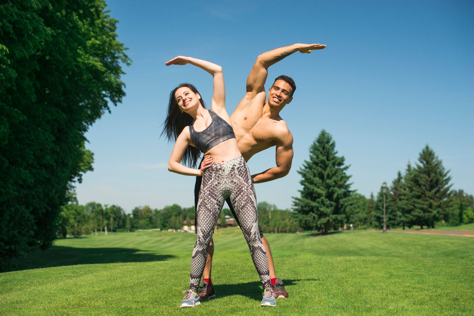 a man and a woman working out together in a garden with trees