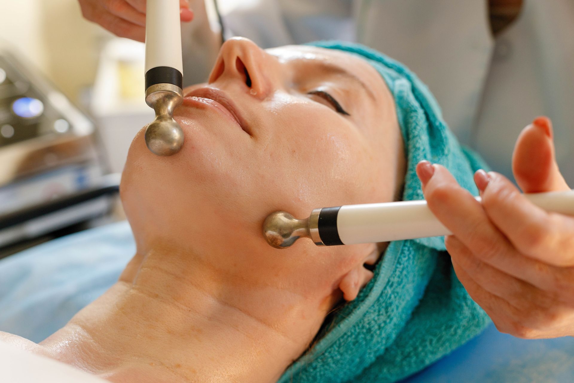 A person receiving a professional microcurrent facial treatment with dual metal-tipped probes on their jawline.