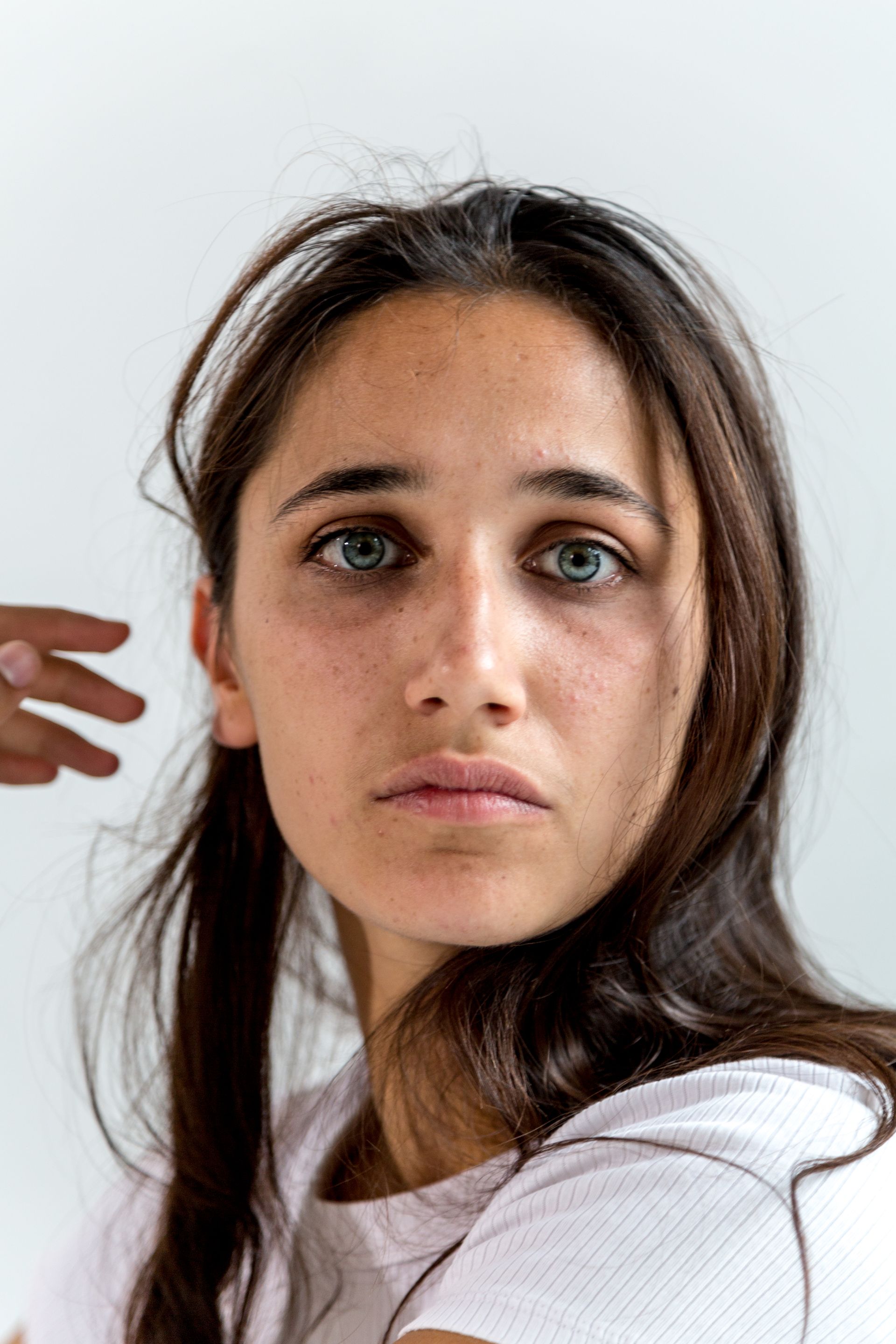Woman with long dark hair looking at the camera against a plain light background.