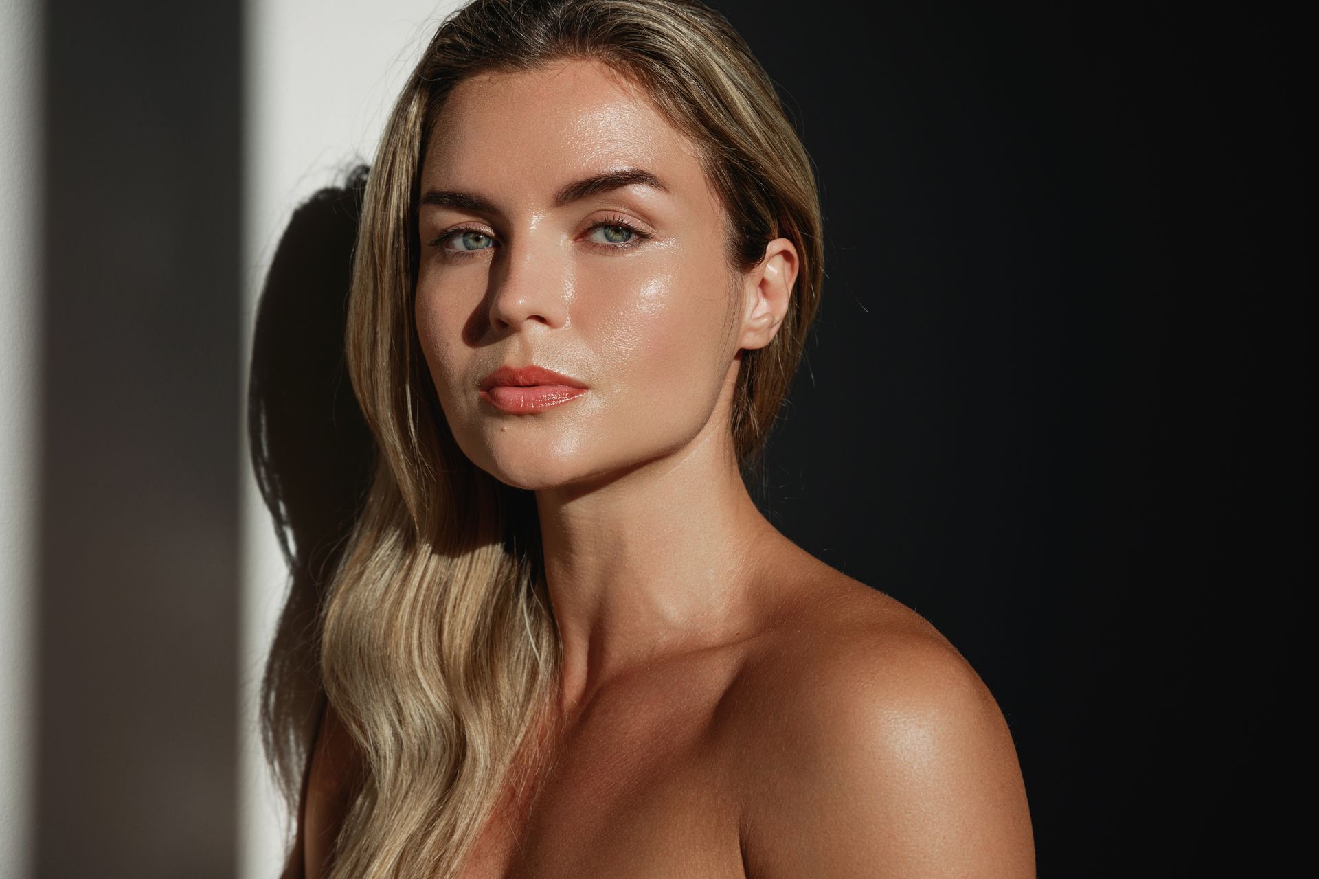 Portrait of a person with long blonde hair against a dark background, gazing at the camera.
