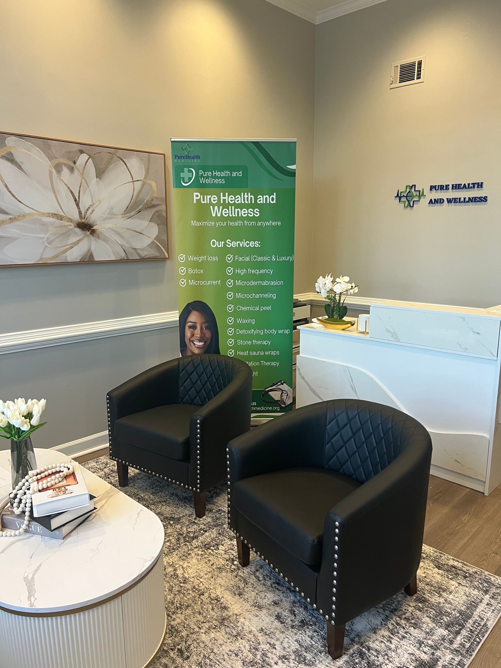 Modern waiting area with two black chairs, round white table, green banner, and floral wall art
