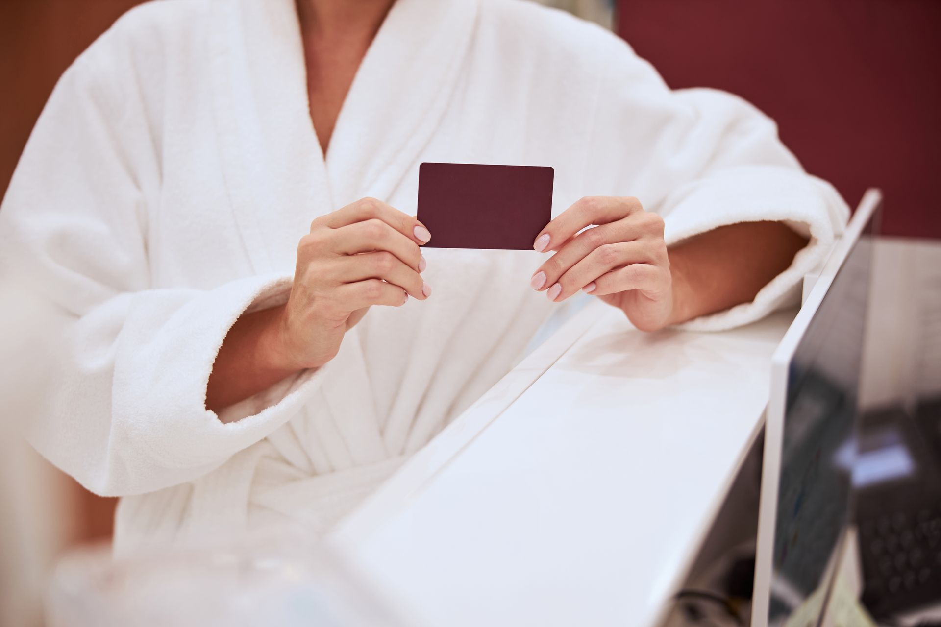 Person in white robe holding a maroon card in front of a mirror