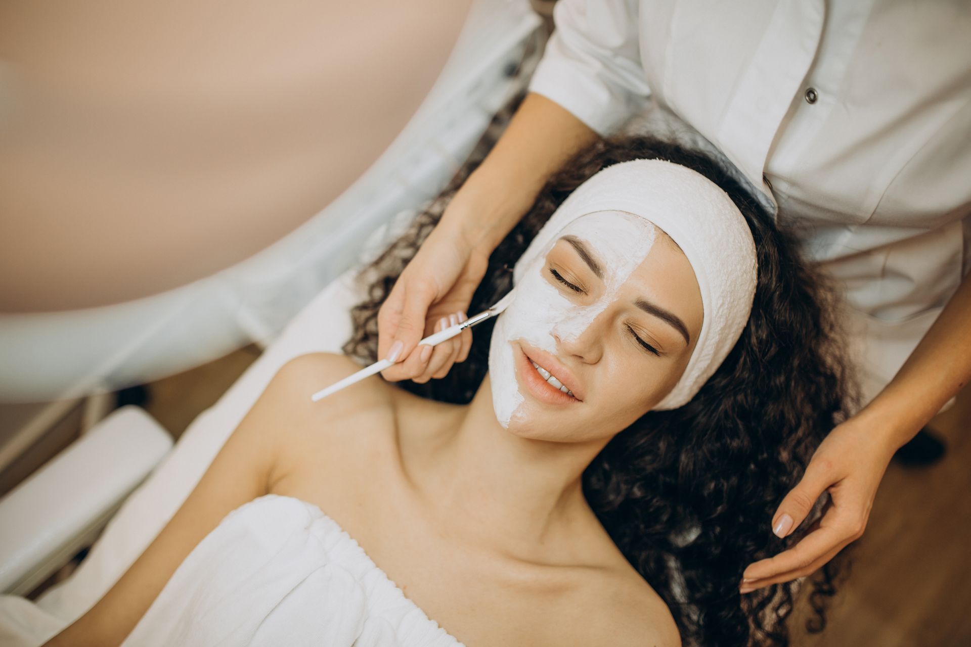 a hand applying a face mask on a woman's face with a brush