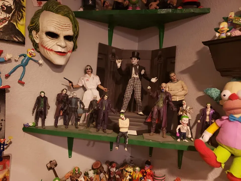A Joker-themed display shelf with various character figures, a mask on the wall, and a Krusty the Clown doll.