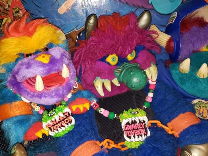 Two colorful, furry My pet monster plush and my pet monster pets with “Gnarly Toybox” necklaces, featuring horns, sharp teeth, and bright, shaggy fur.