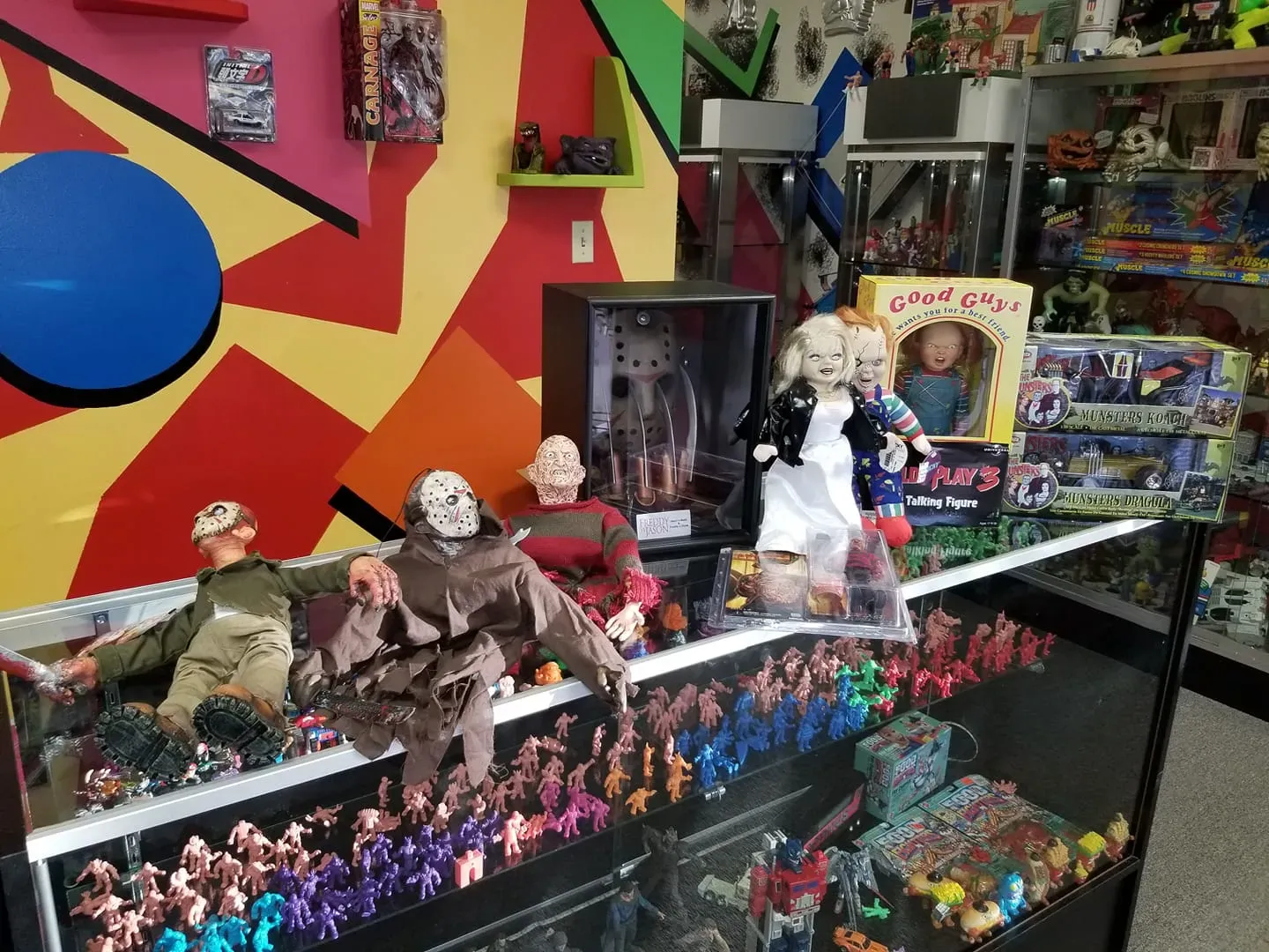 A display case filled with horror movie action figures and dolls, including Jason and Chucky, inside a colorful store.