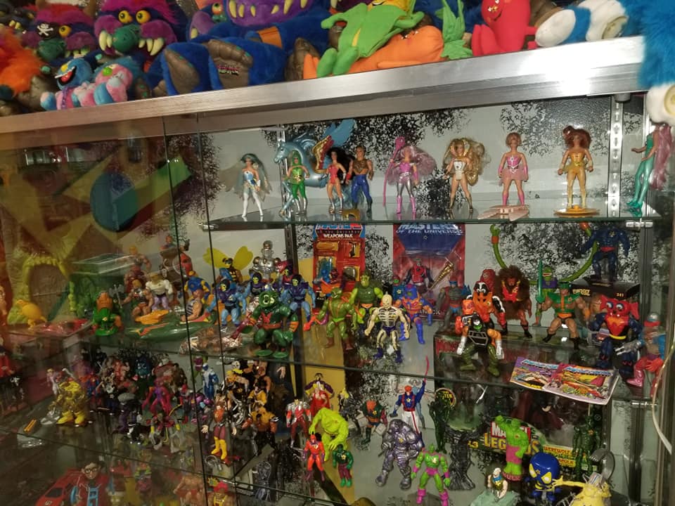 A glass display case filled with a large collection of colorful action figures and plush monster toys on shelves.