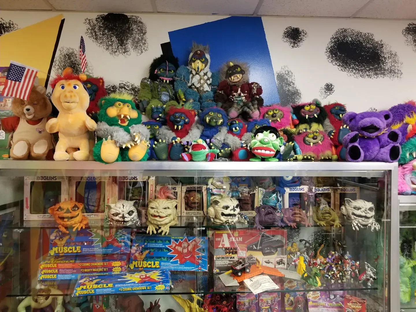 A glass display case filled with a variety of colorful vintage plush toys and small action figures.
