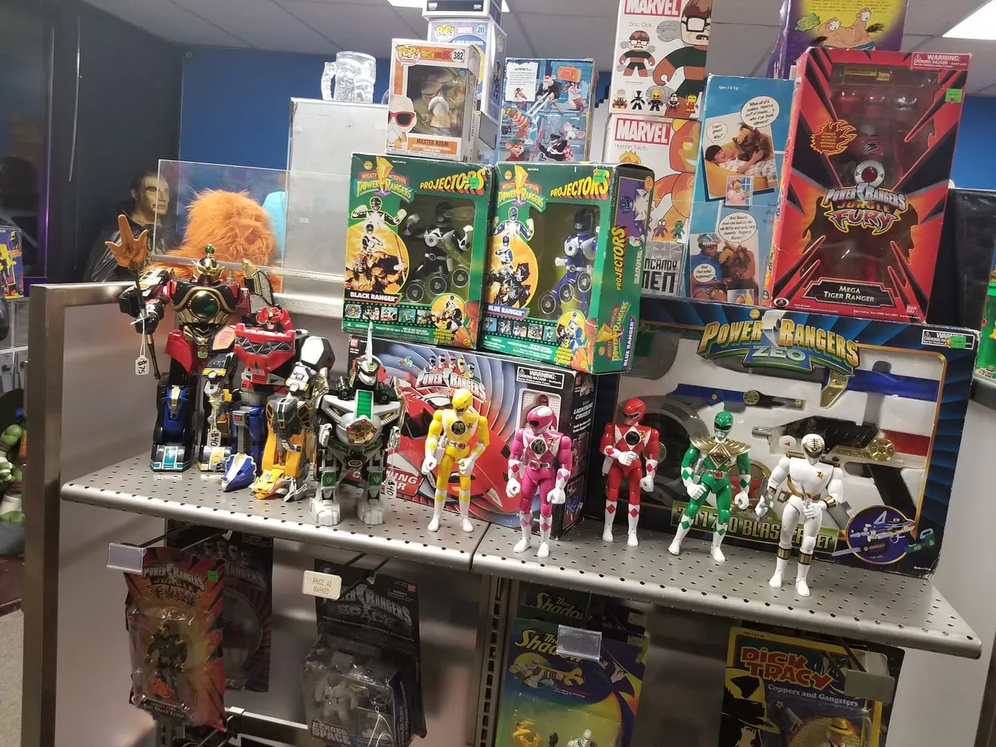 A display shelf filled with Power Rangers action figures, boxed toys, and collectibles in a retail store setting.