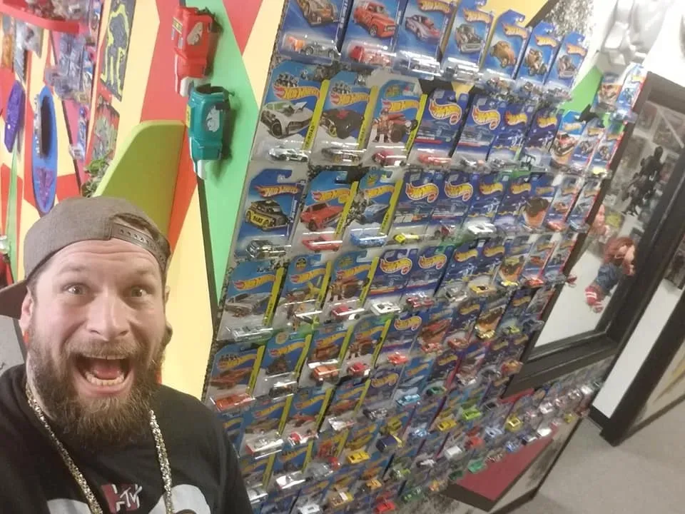 Brandon the founder of The Gnarly Toybox in front of a wall covered in many packaged Hot Wheels toy cars.