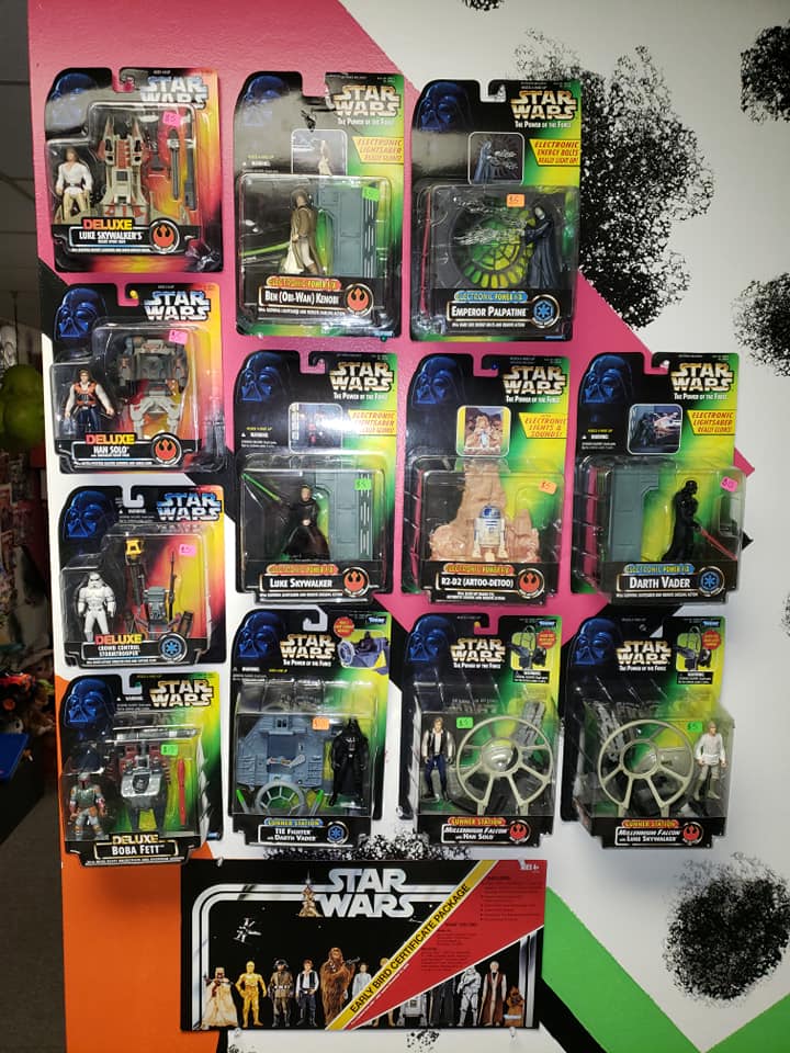 A display of twelve packaged Star Wars action figures on a wall, with a promotional poster underneath.