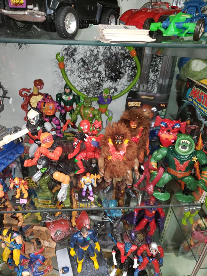 A display shelf filled with various vintage Masters of the Universe and Marvel action figures.