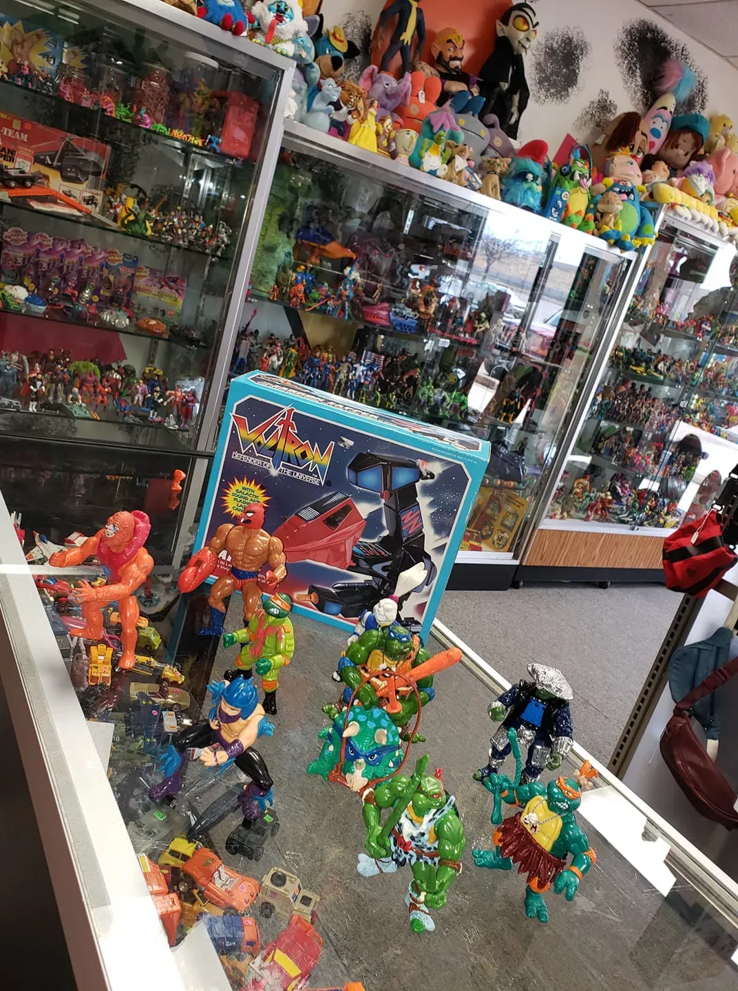 A display case filled with assorted action figures and vintage toys inside a retail shop.