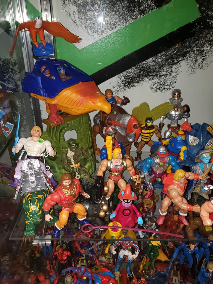 A shelf filled with assorted colorful Masters of the Universe action figures and vehicles, including a bird-shaped ship.