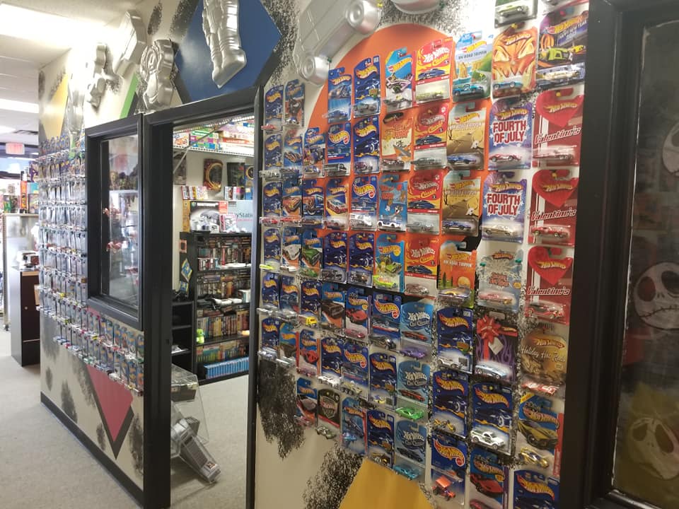 A shop wall displaying a large collection of packaged Hot Wheels toy cars arranged in vertical rows.
