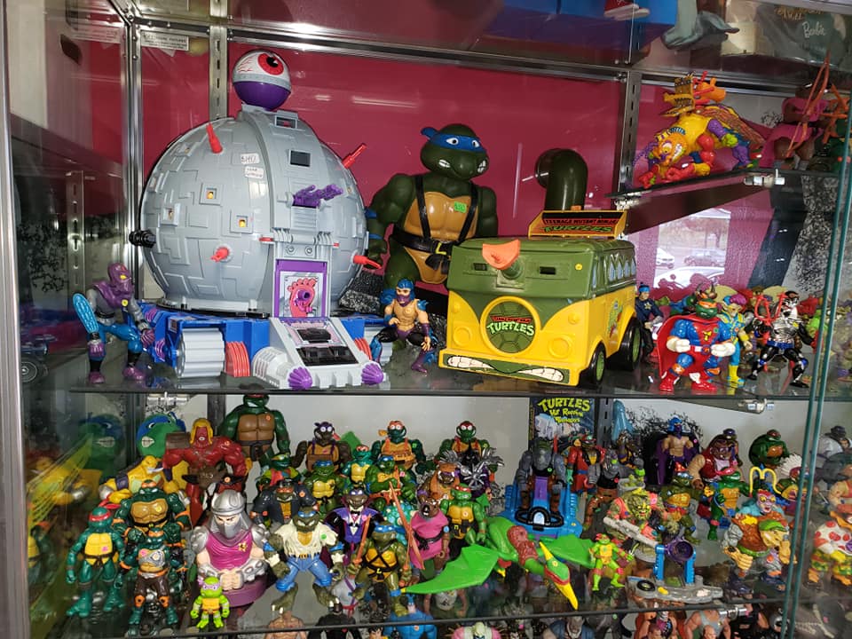 A display case filled with a collection of vintage Teenage Mutant Ninja Turtles action figures, vehicles, and playsets.