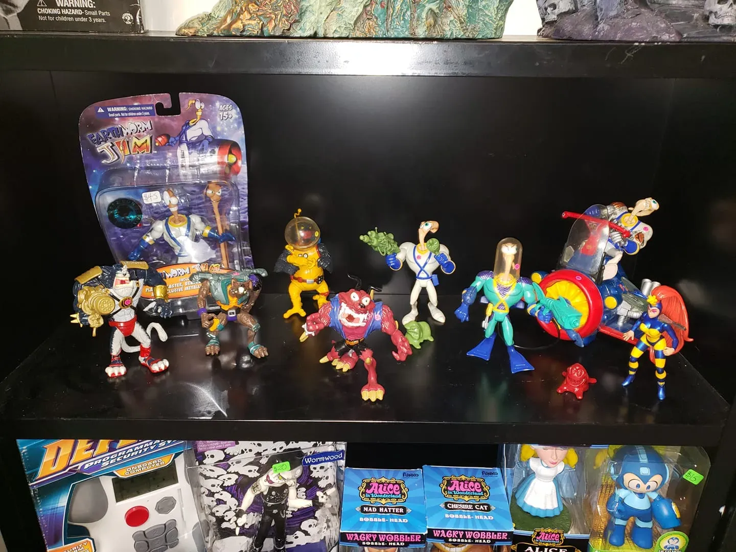 A shelf displays a collection of colorful plastic action figures, including character sets from Space Jam and Mega Man.
