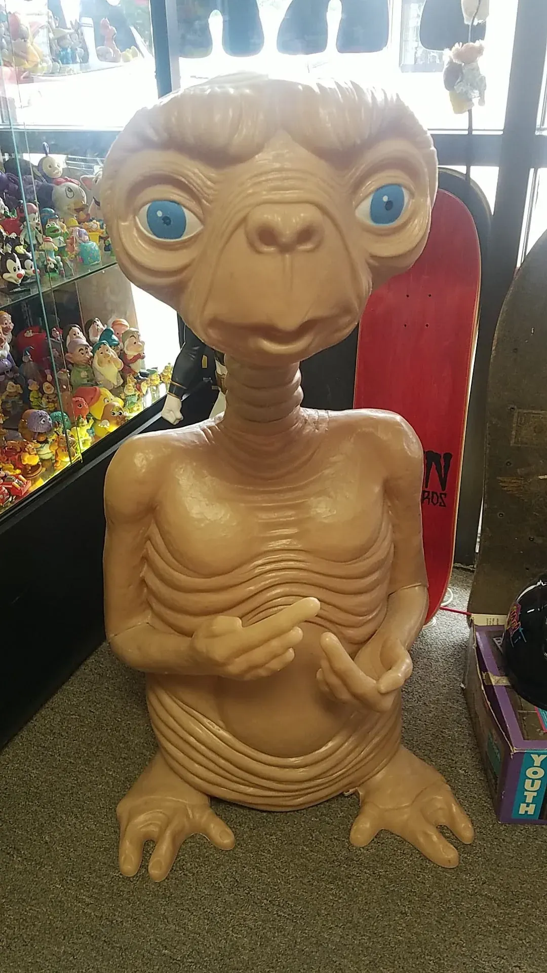 A tan E.T. the Extra-Terrestrial figure with large blue eyes, standing on display in a retail store.