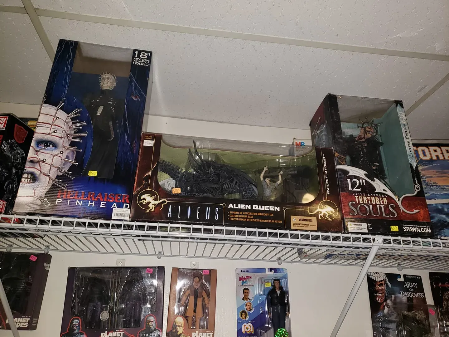 A shelf filled with boxed horror movie action figures, including Pinhead, Alien Queen, and various other collectible dolls.