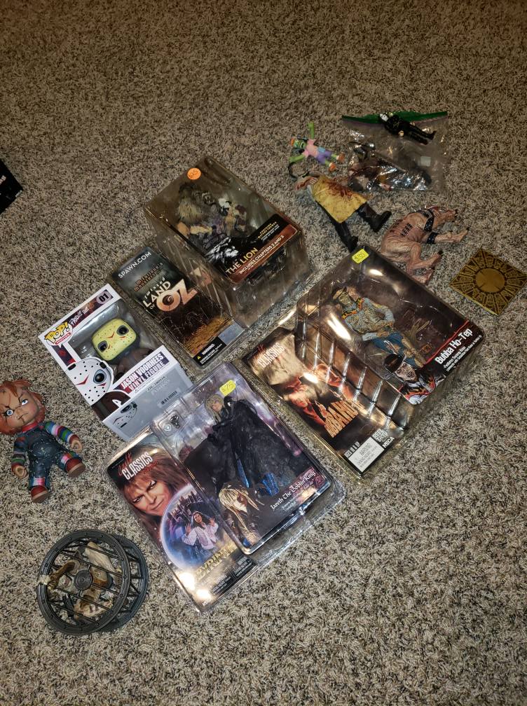 A collection of horror-themed action figures, Funko Pops, and a puzzle box scattered on a carpeted floor.
