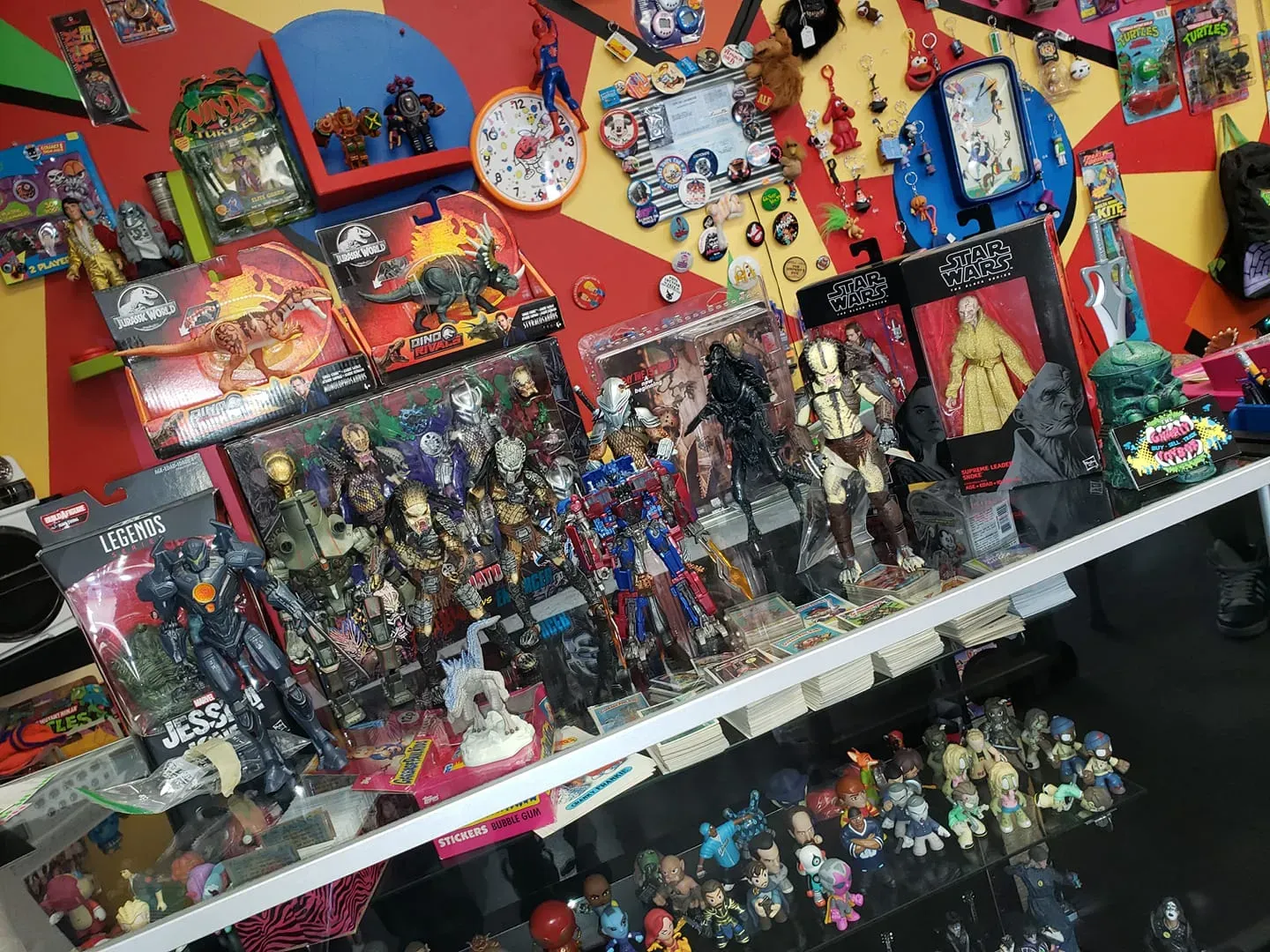 Display shelves filled with various collectible action figures and toys against a vibrant, multi-colored geometric wall.