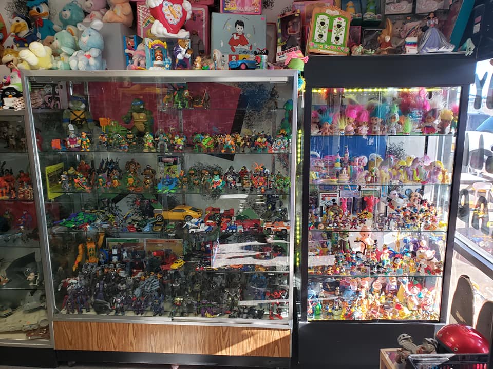 Two glass display cases filled with vintage action figures, dolls, and plush toys in a shop setting.