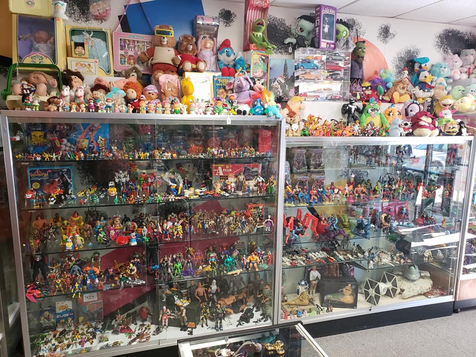 Glass display cases filled with assorted toy figures, with many plush toys arranged on top in a collector's store.