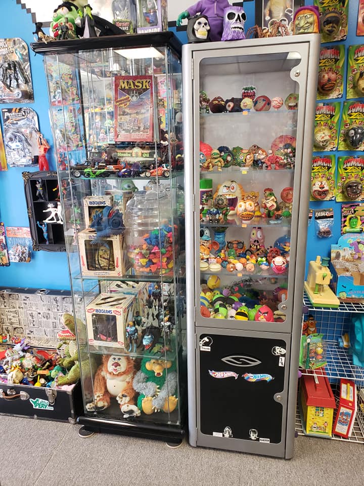 Two glass display cases filled with toys, figurines, and collectibles against a bright blue wall in a shop.