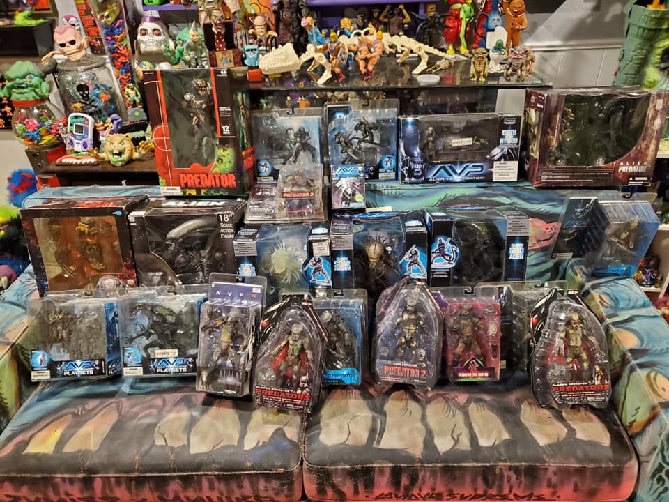 A collection of Alien and Predator action figures in their original packaging, displayed on a textured patterned couch.