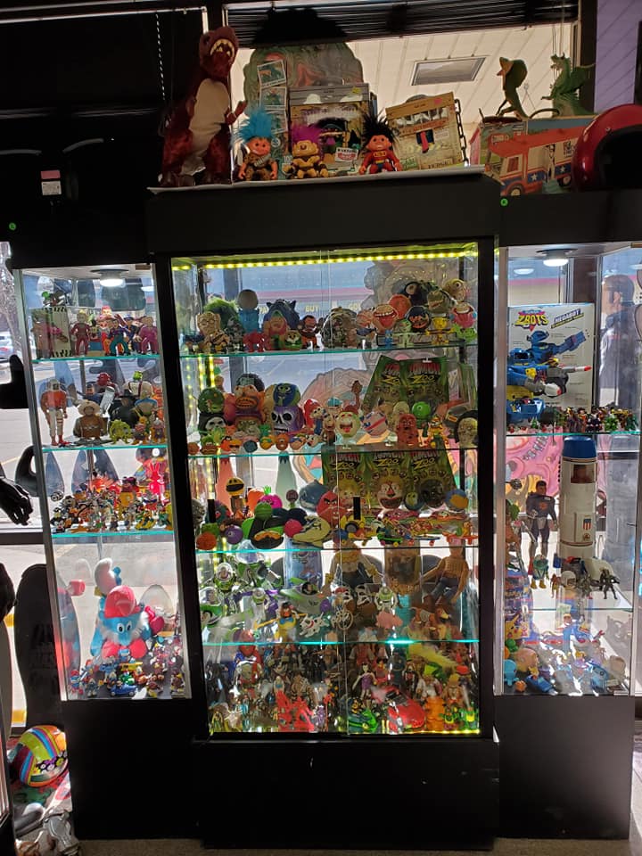 Three display cabinets filled with numerous small collectible figurines and toys, illuminated with green LED lights.