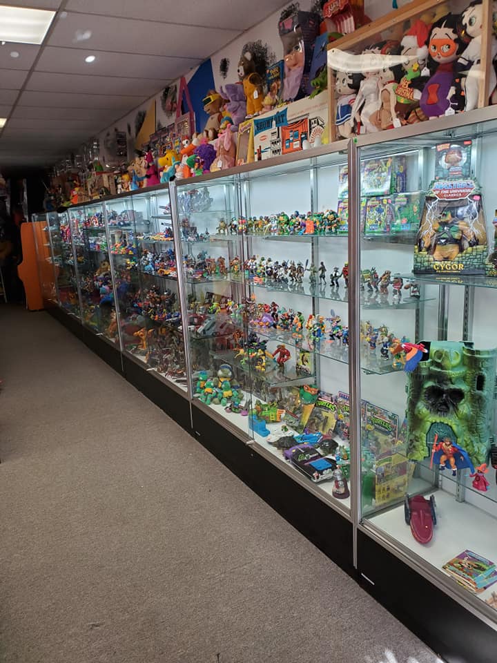 A long row of glass display cases filled with vintage collectible toys and action figures inside a retail store.