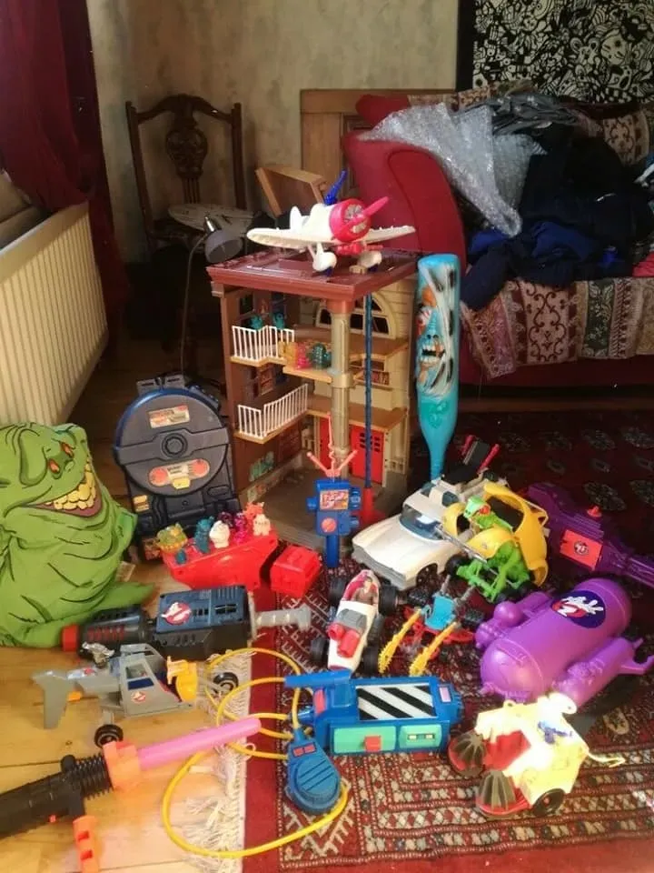 A collection of assorted vintage Ghostbusters toys and playsets scattered on a patterned rug in a living room.
