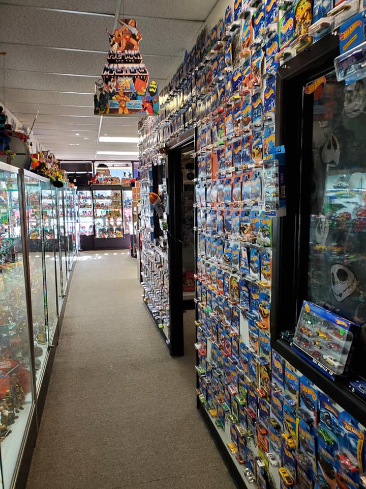 A narrow hallway in a shop with walls covered in packaged Hot Wheels cars and a display case along the left wall.