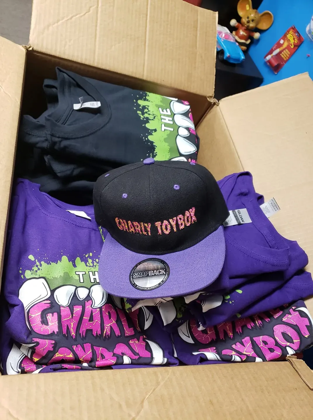 A box containing folded black and purple T-shirts with