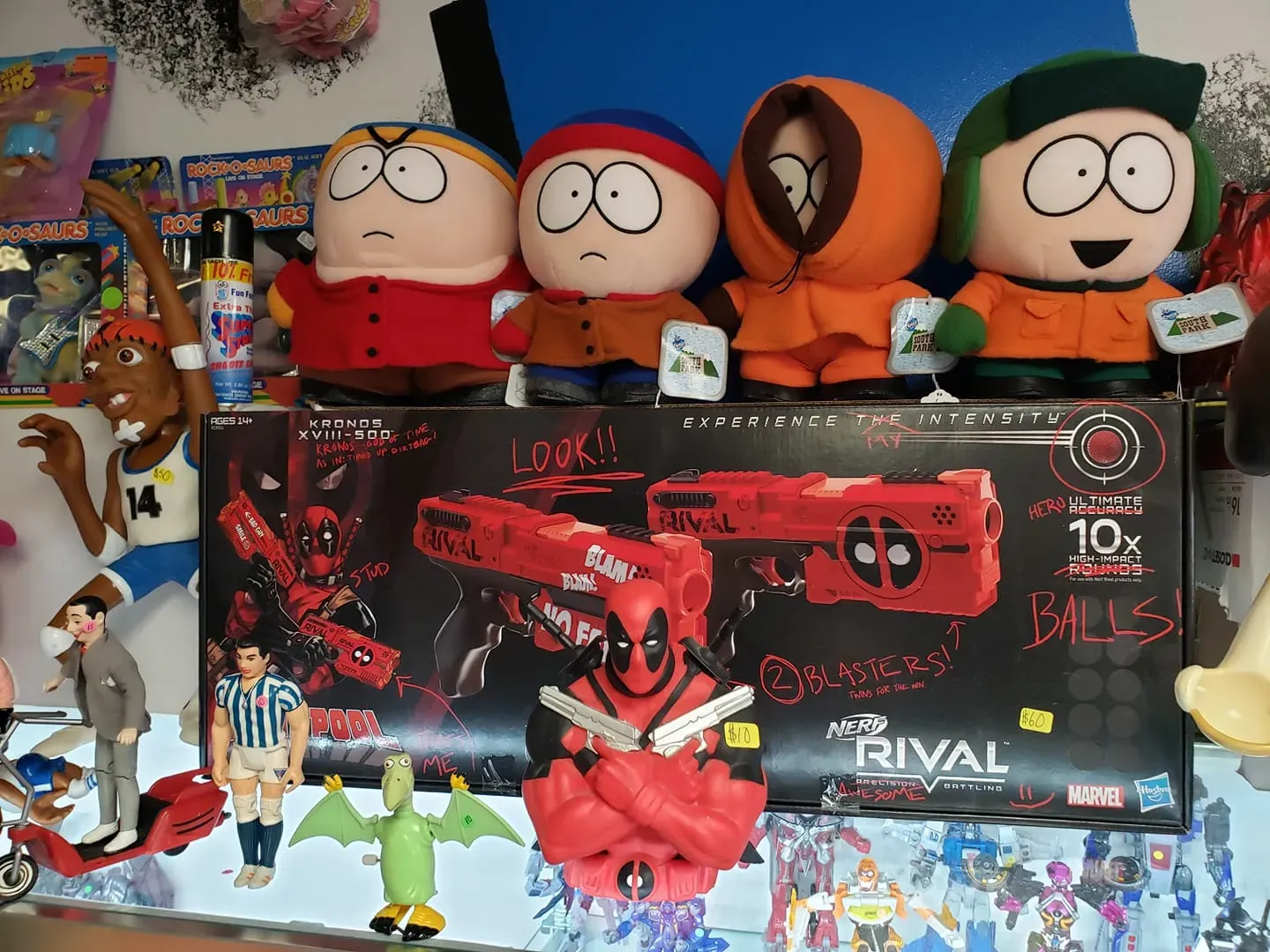 Plush South Park characters sit atop a Deadpool-themed Nerf Rival blaster box, surrounded by various action figures.