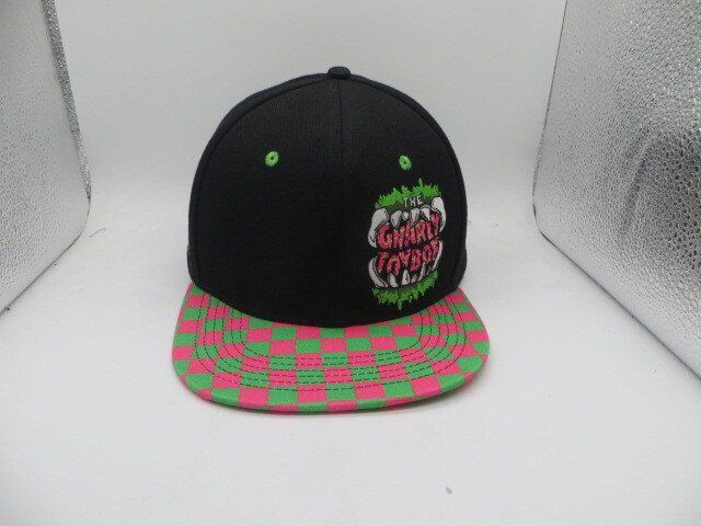 Black baseball cap with a green and pink checkered brim and an embroidered monster-mouth graphic reading 