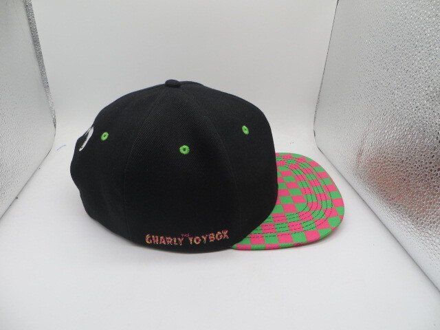 A black baseball cap with green eyelets and a pink and green checkered brim, featuring the text 
