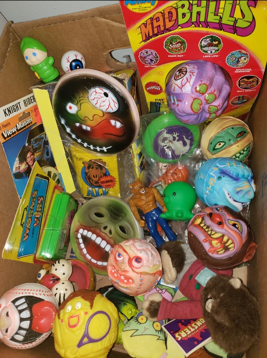 A box filled with assorted vintage toys, including various Madballs, small action figures, and colorful collectibles.