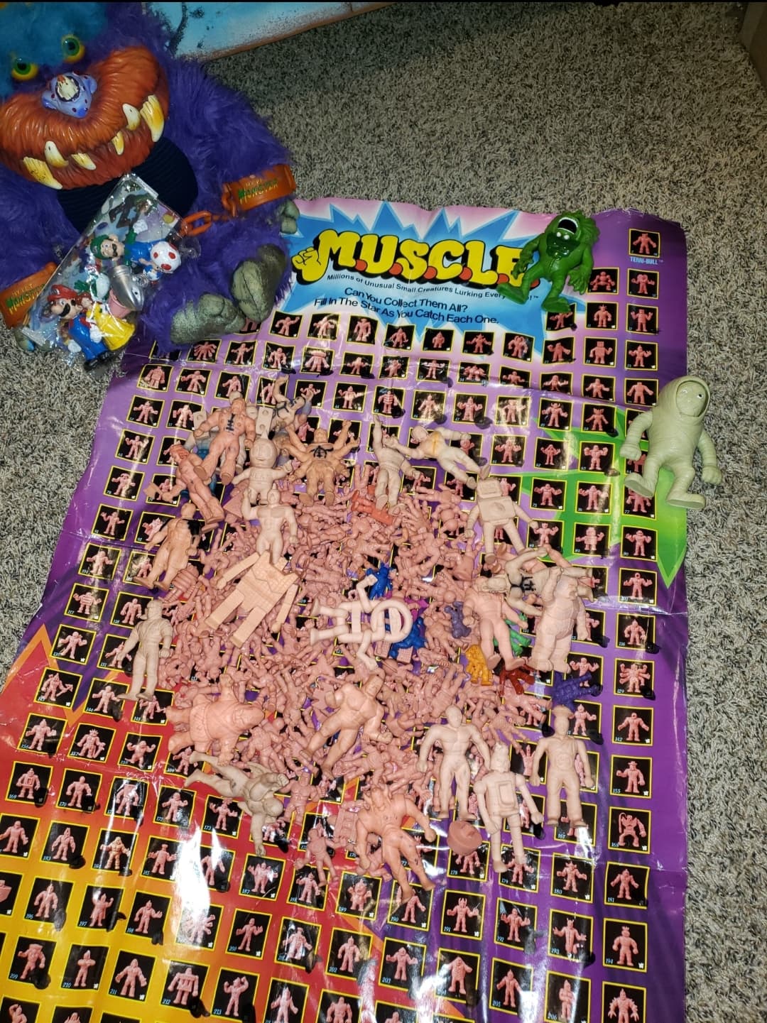 A large collection of small, peach-colored M.U.S.C.L.E. wrestling figures spread out on a branded collector's poster with Beastuer My pet monster.