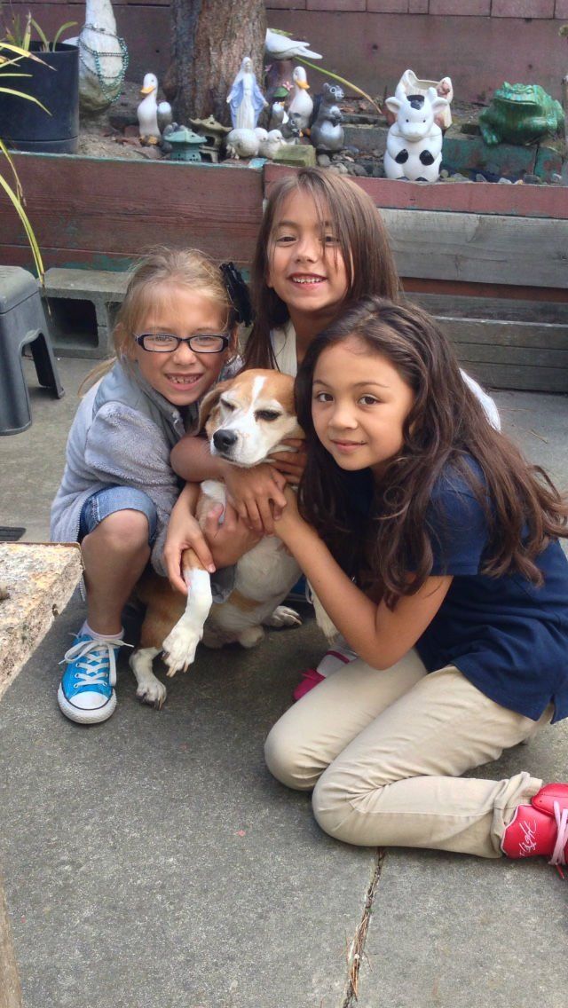 Three children kneeling with a small dog on a patio. The children are smiling.