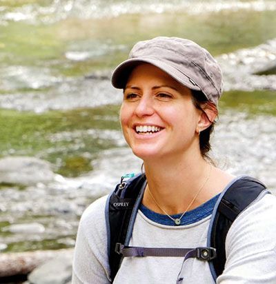 Smiling hiker wearing a cap and backpack beside a rocky stream