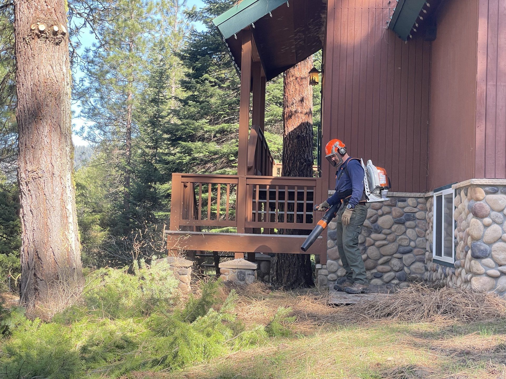 Person with leaf blower near a cabin porch in a wooded area