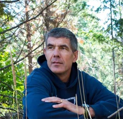 Man in a navy hoodie resting on a bench in a sunlit forest