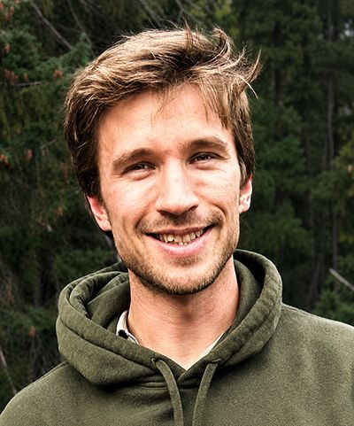 Smiling man in a green hoodie outdoors with mountains in the background