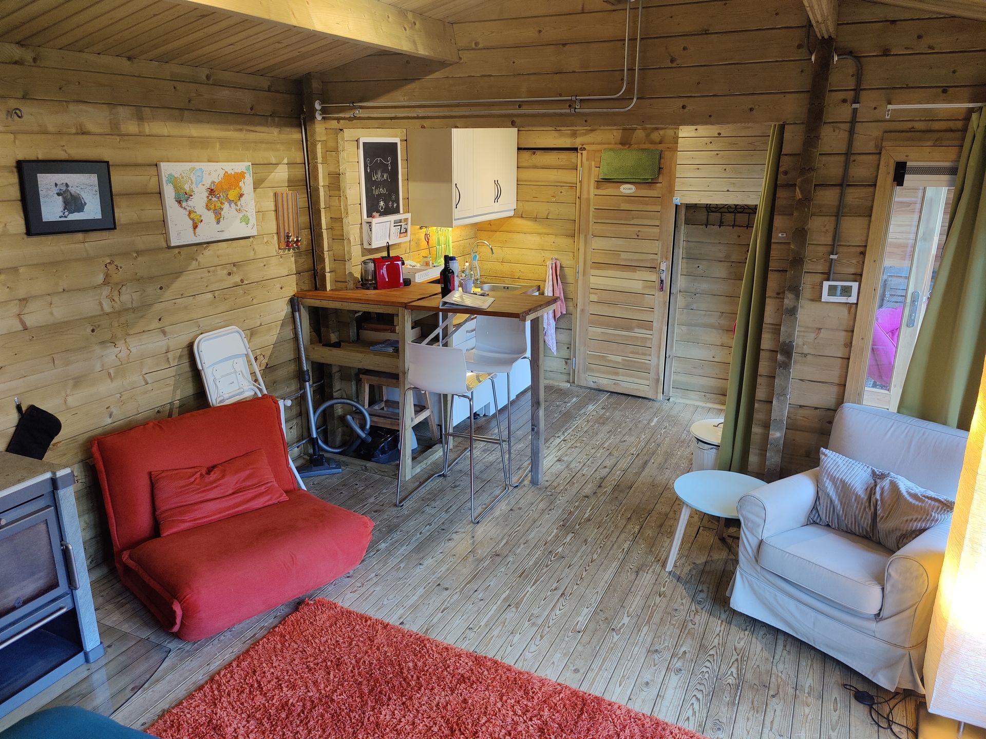 Gezellig interieur van een blokhut met houten lambrisering, een kleine keuken, een rode stoel.