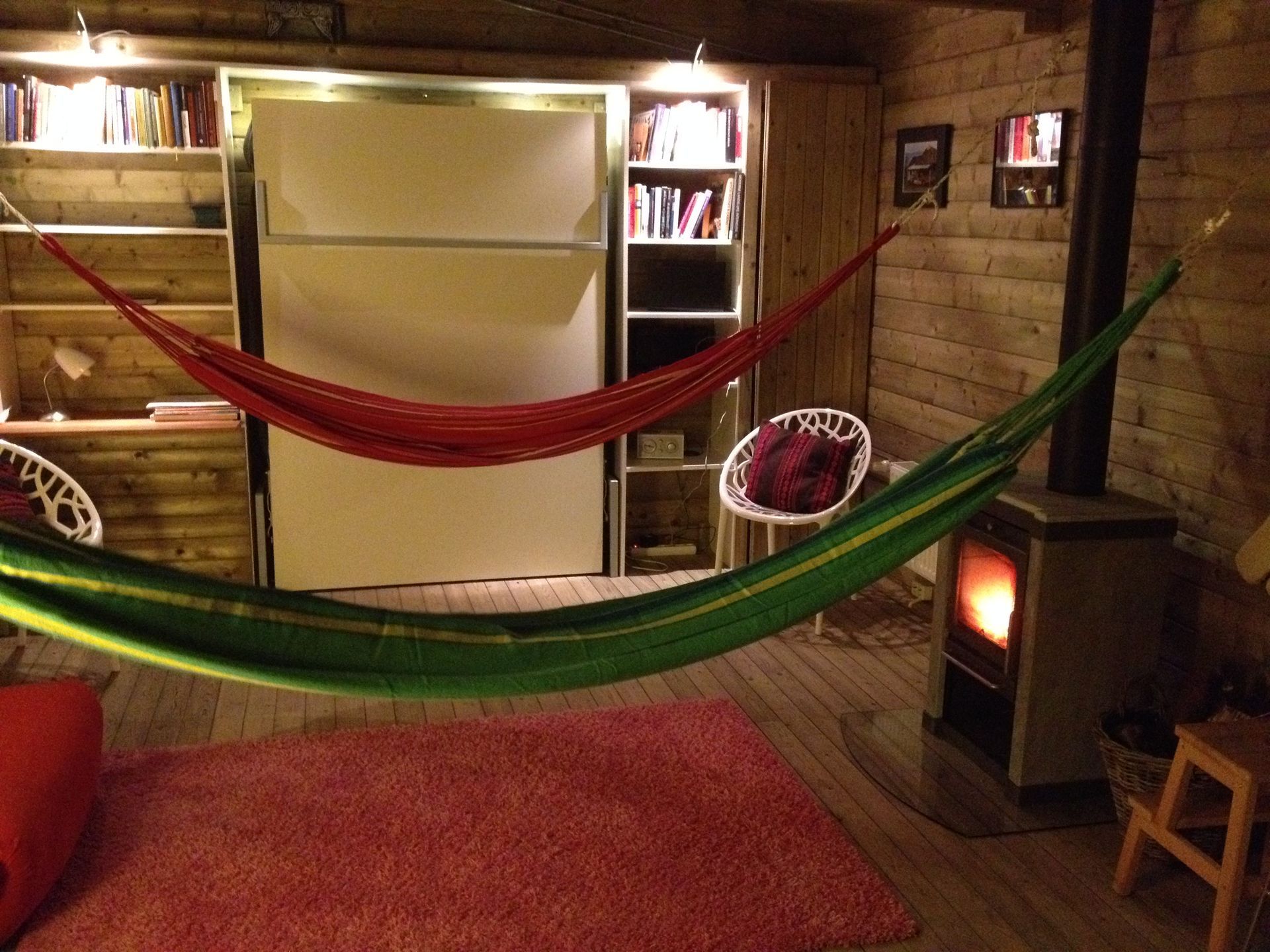 Gezellige houten kamer met twee hangmatten, boekenplanken, een vloerkleed en een kleine houtkachel.