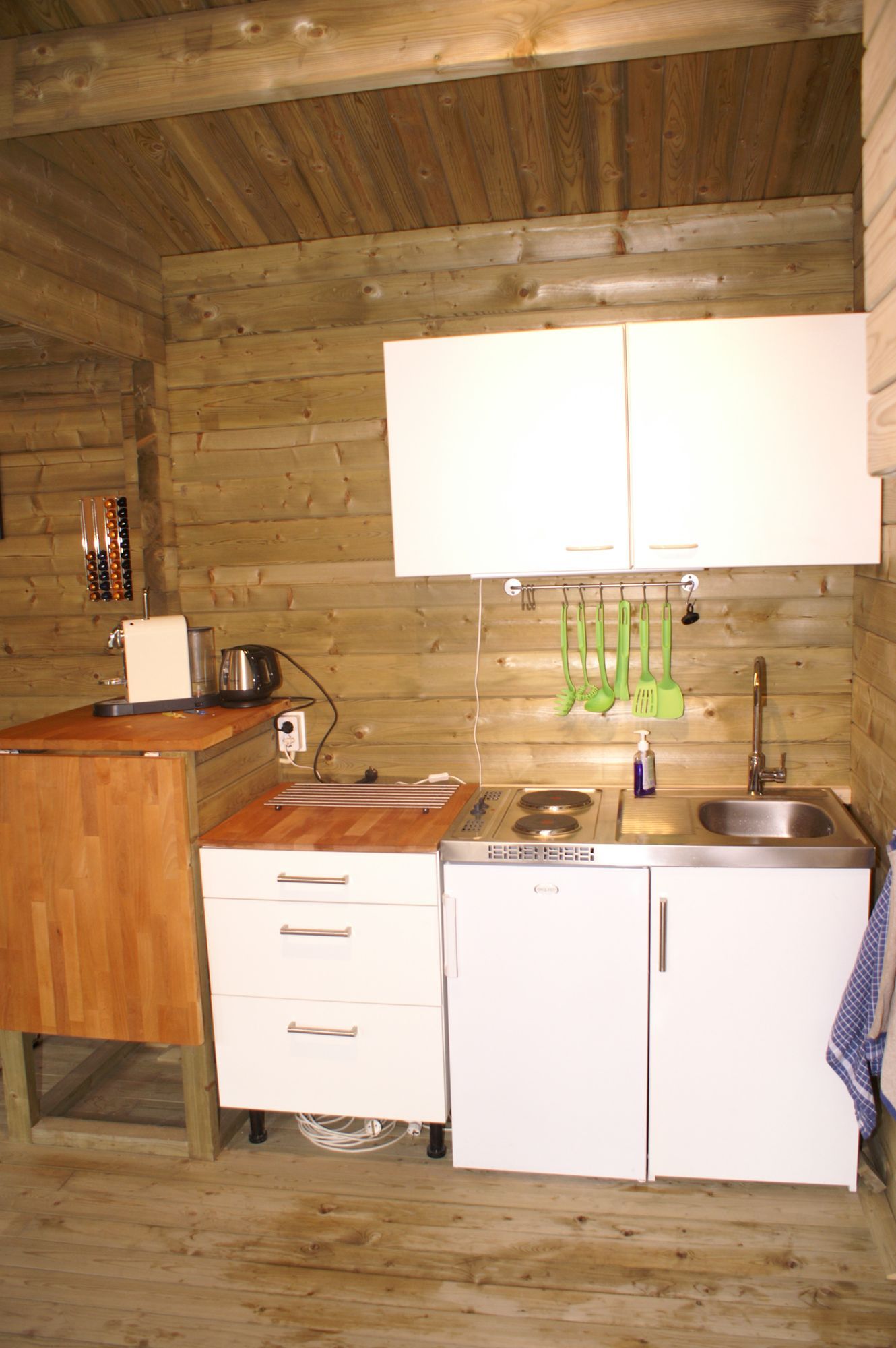 Kleine, rustieke keuken met houten wanden, witte kastjes, een spoelbak en een aanrechtblad aan de linkerkant.