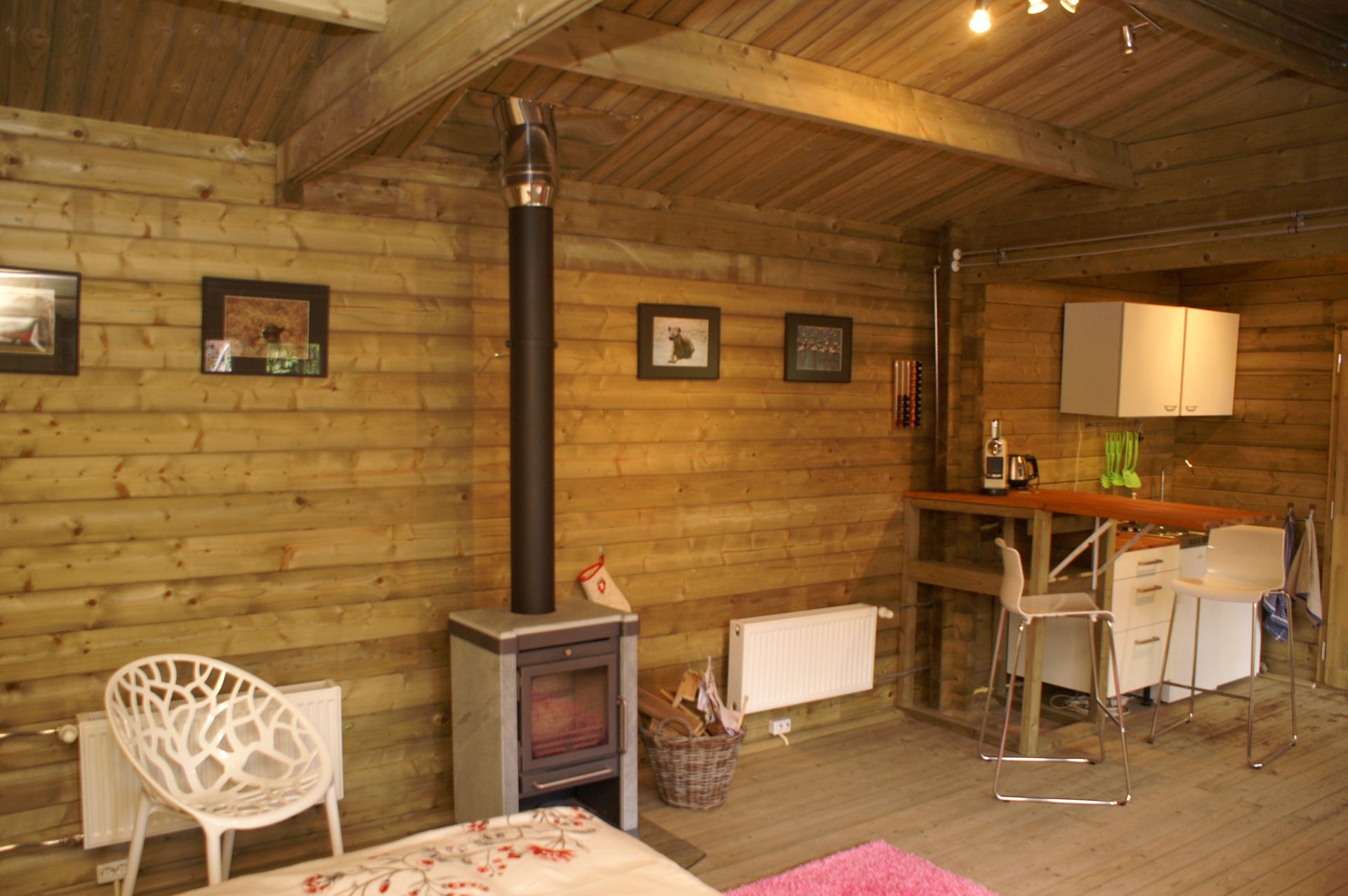 Houten interieur met een houtkachel, een kleine eethoek en een witte stoel onder warme verlichting.